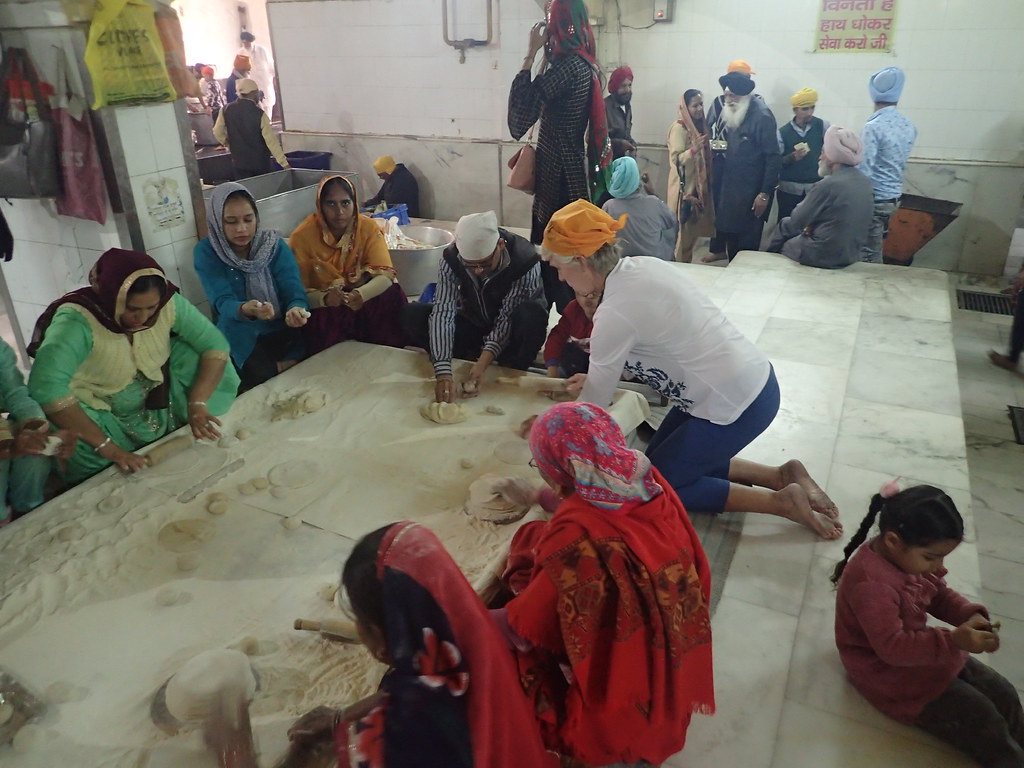 A group of women and men seated on a floor, rolling rotis together in a community kitchen