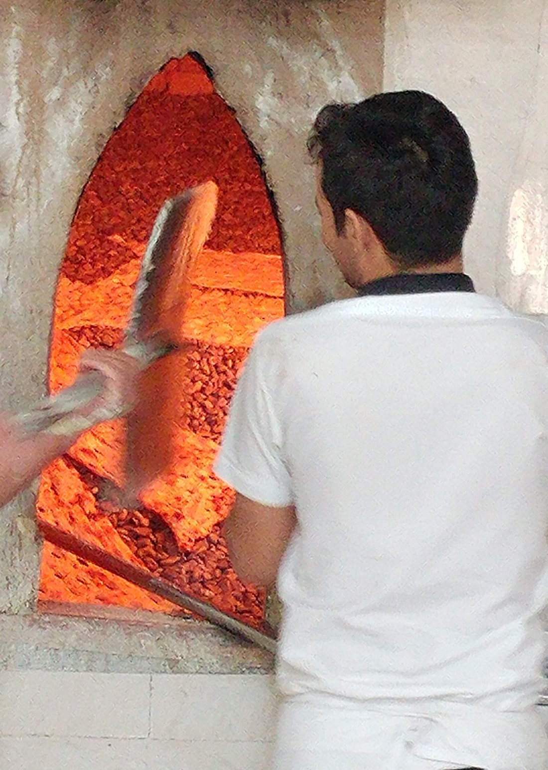 A baker working a long peel at the mouth of a sangak oven whose floor is a bed of glowing pebbles
