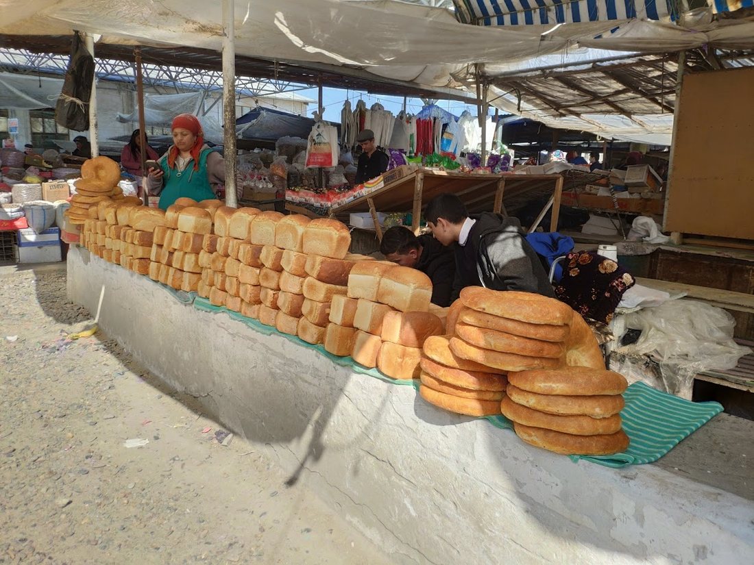 A long market counter stacked with round Uzbek non, vendors behind it under an awning