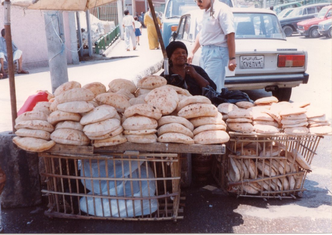 A street vendor in Cairo seated behind a table and crates piled high with round, puffed flatbreads