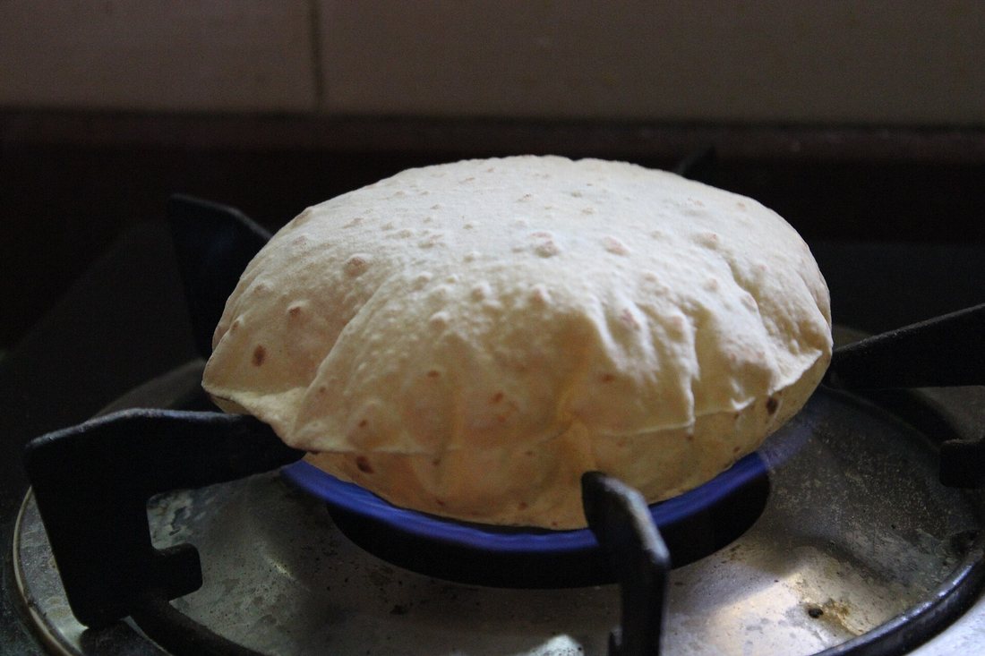 A roti puffed into a round ball, sitting directly on the flame of a gas burner