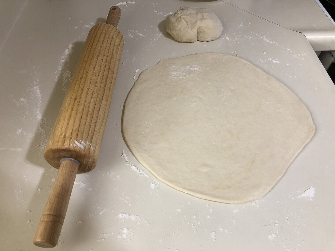 A thin round of rolled dough beside a wooden rolling pin and a ball of dough on a floured counter