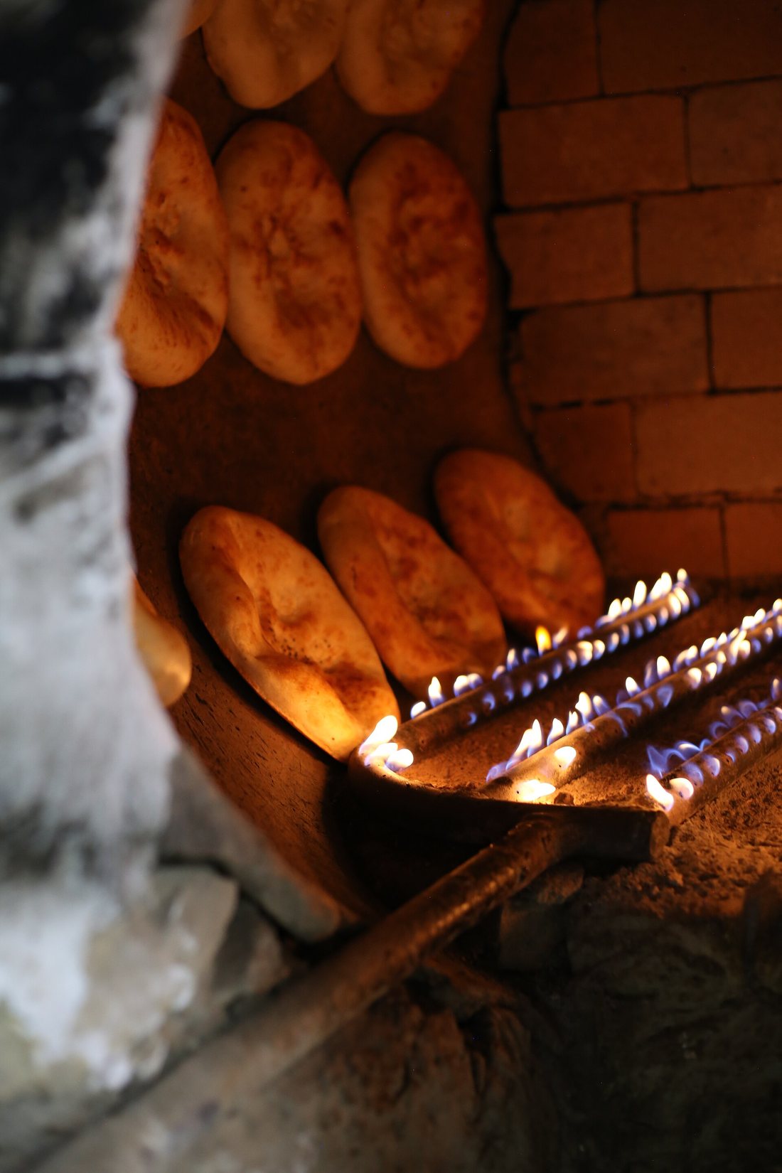 Inside a gas-fired tandir: rows of round Uzbek non stuck to the curved oven wall above the burner flames