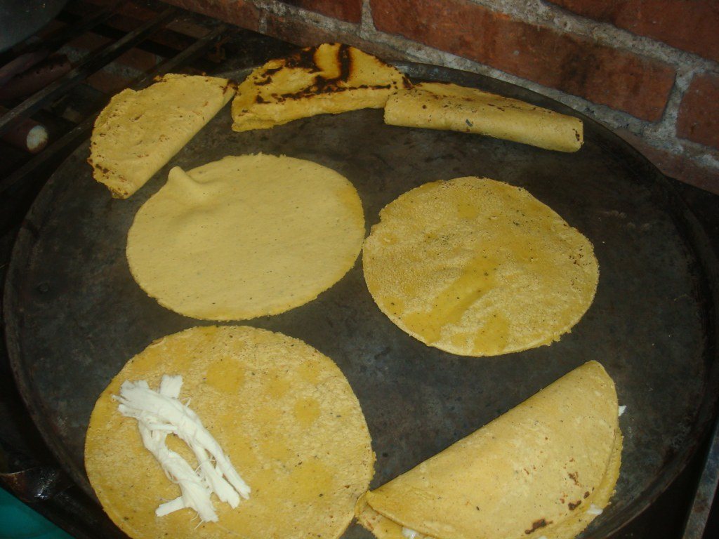 Yellow corn tortillas and folded quesadillas cooking on a round dark comal