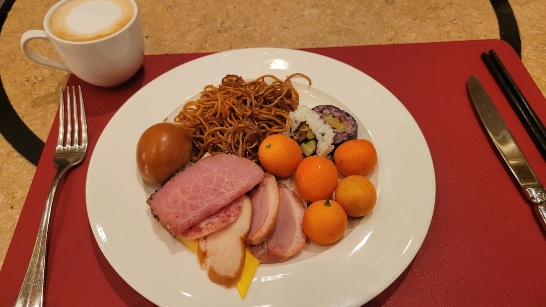 Fried noodles, ham, a nori roll, kumquats and a coffee — the two traditions on one plate, which is what actually happens