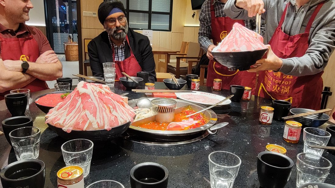 The sliced meat arriving — a mounded platter of paper-thin beef, carried in and presented before any of it goes near the pot