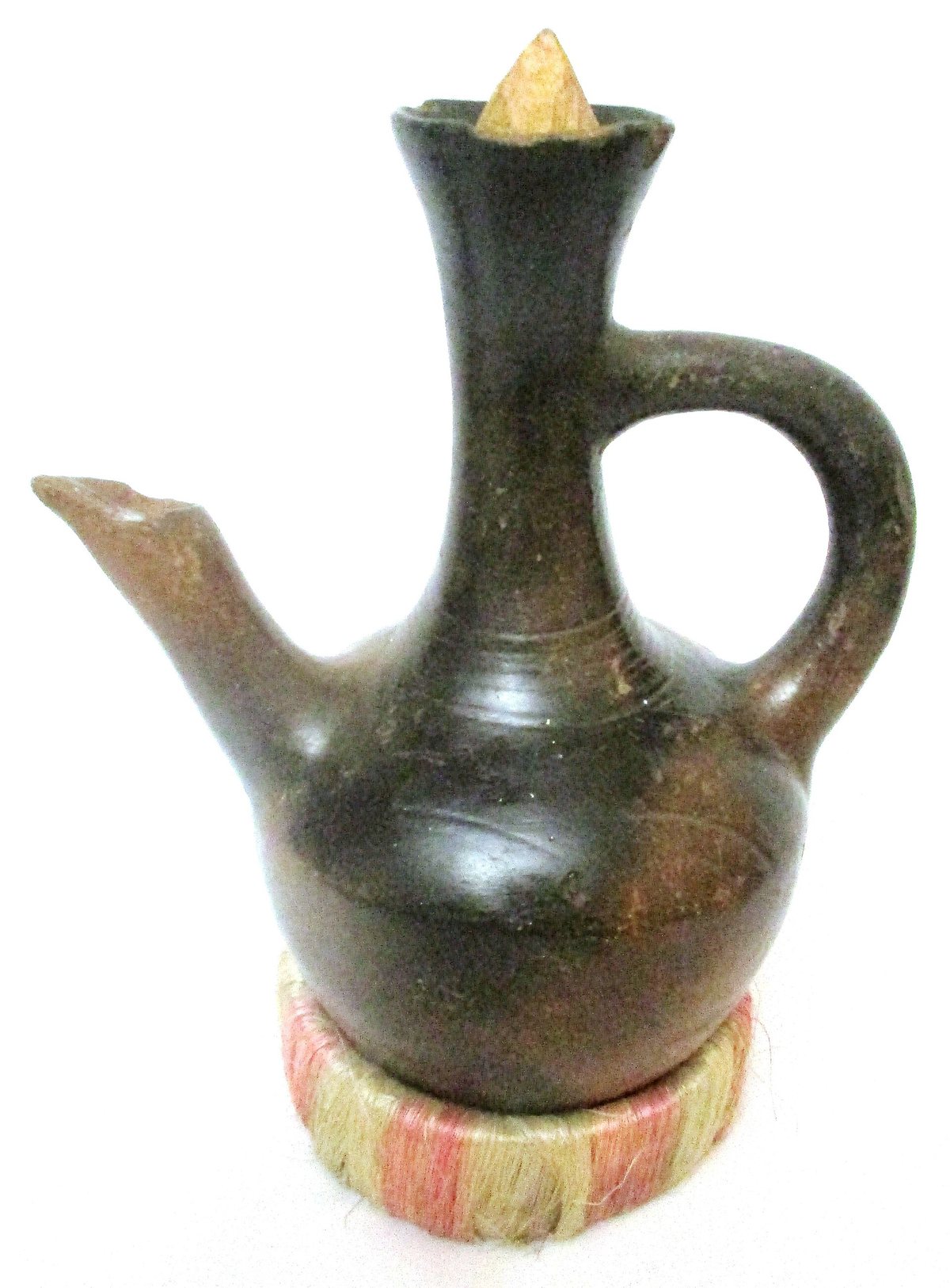 A clay jebena on its woven ring stand — the round belly sits in the coals, and the long neck is the filter
