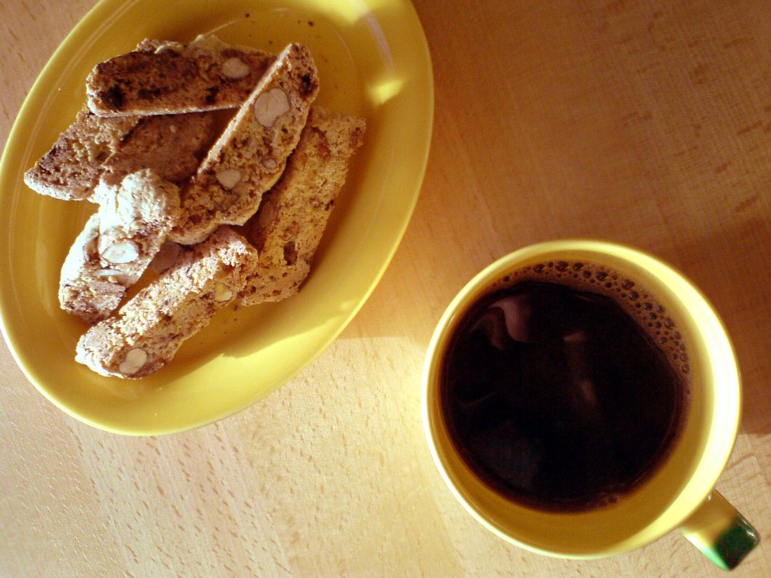 Biscotti on a yellow plate beside a cup of black coffee