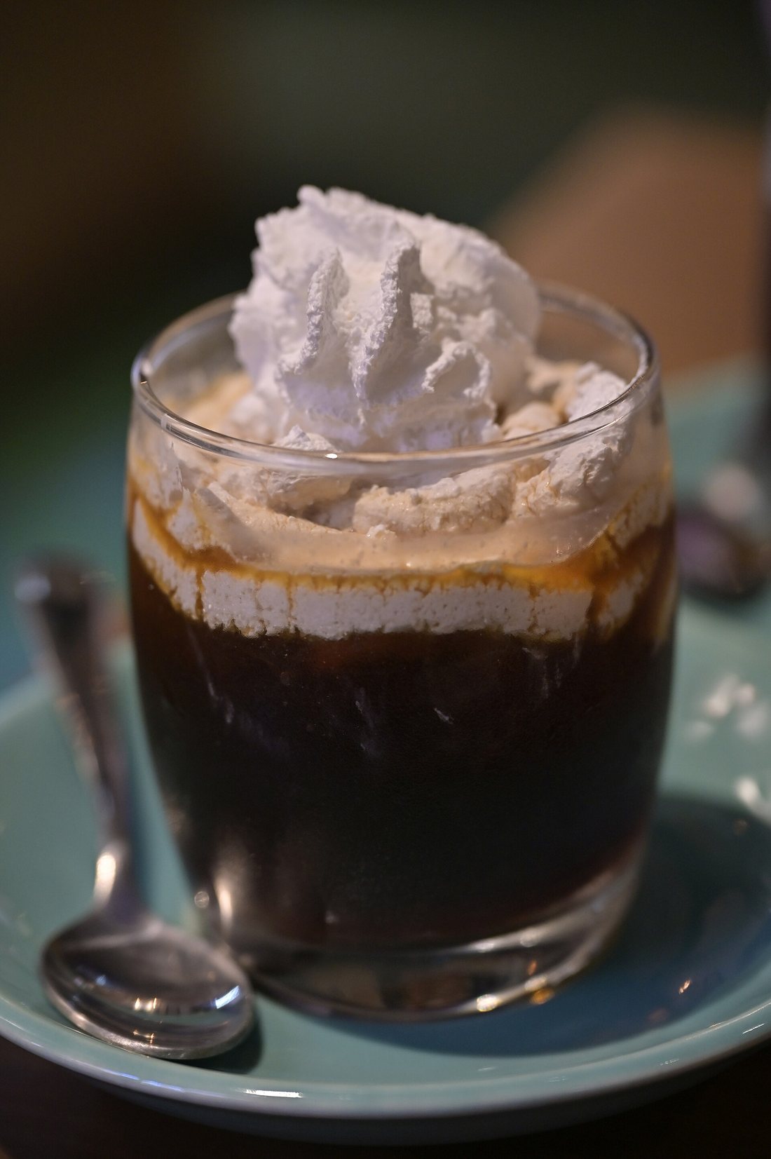 A glass of cold brew topped with whipped cream, on a saucer with a spoon