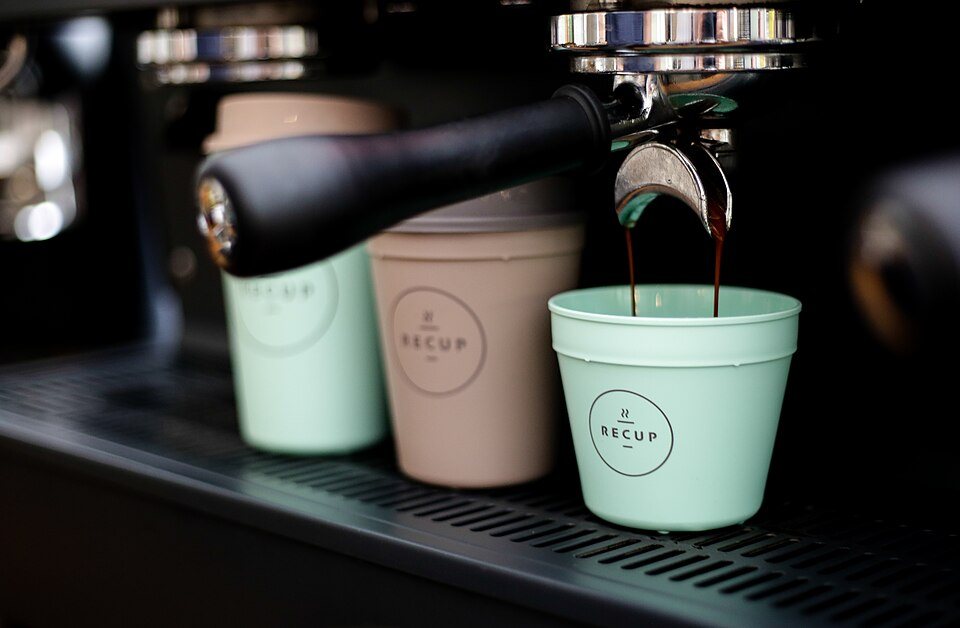 Three pastel reusable cups in different sizes under the spouts of an espresso machine, one catching a shot