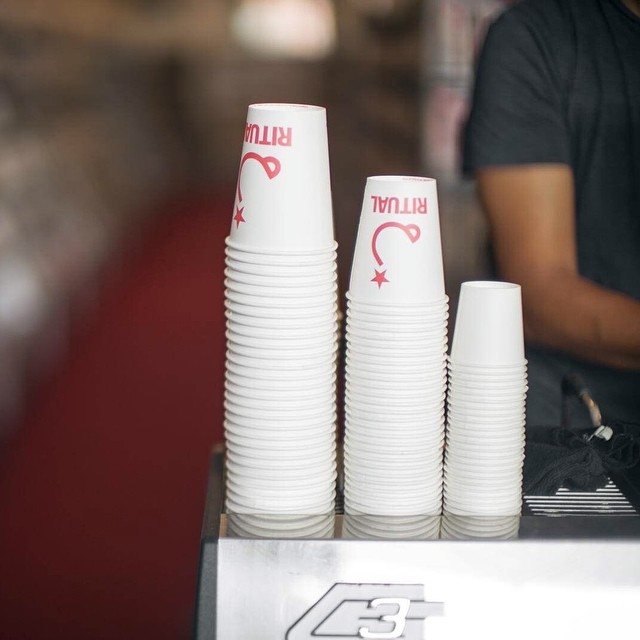Three tall stacks of white paper cups, two of them printed with a red logo, on a café counter