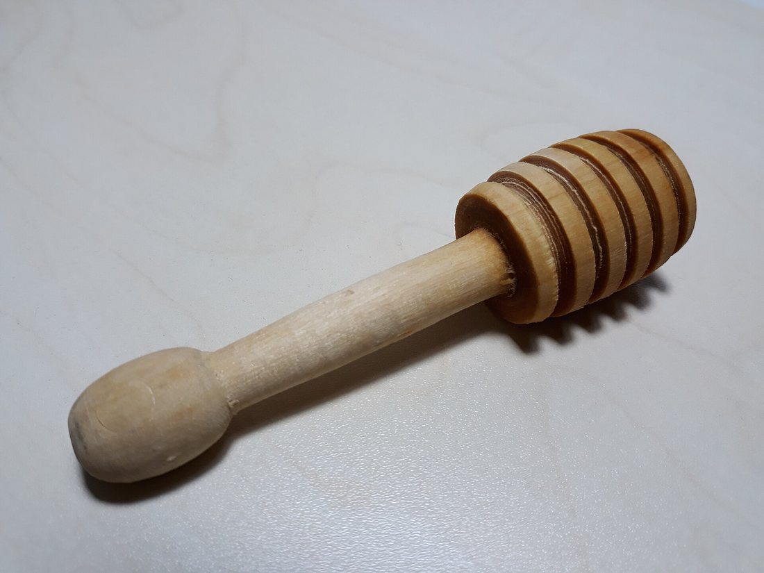 A turned wooden honey dipper on a white surface