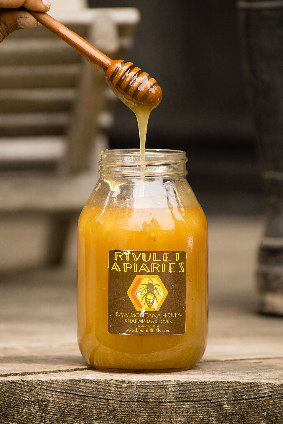 Thick honey running off a wooden dipper into a jar