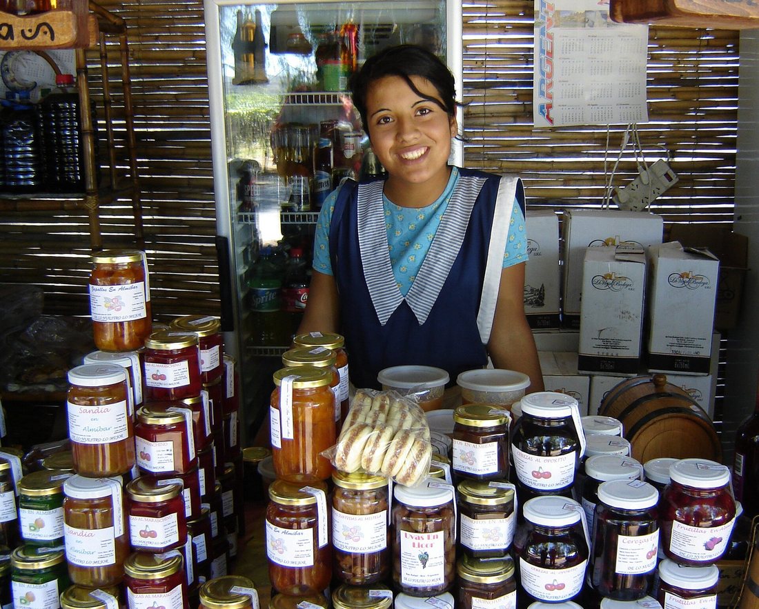 A woman behind a market table stacked with jars of jam