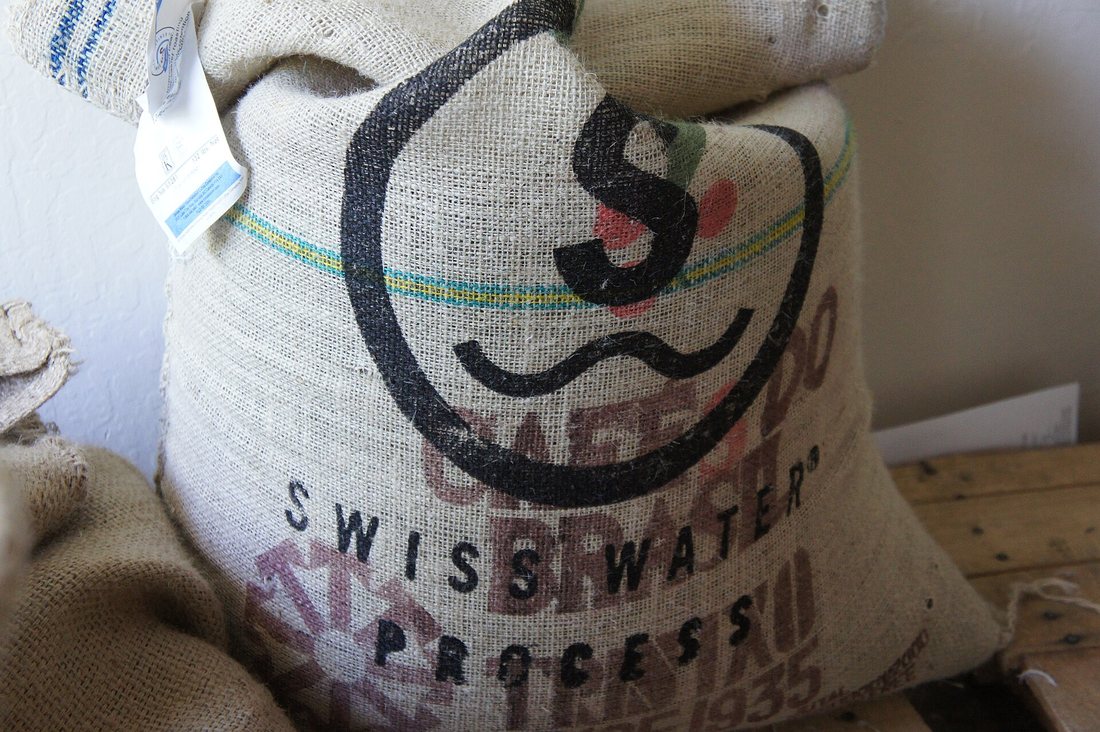 A burlap sack of green coffee printed with the Swiss Water Process mark