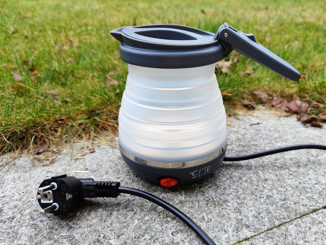 A small folding electric travel kettle standing on a stone step outdoors, its cord beside it