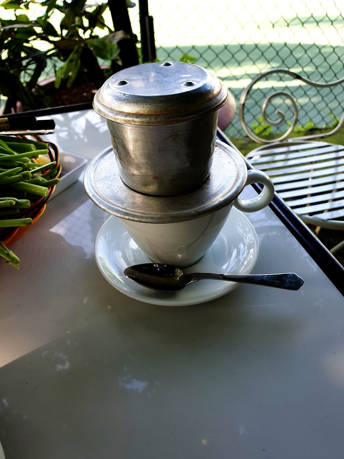 A metal phin filter sitting on a white cup on a café table, coffee dripping through