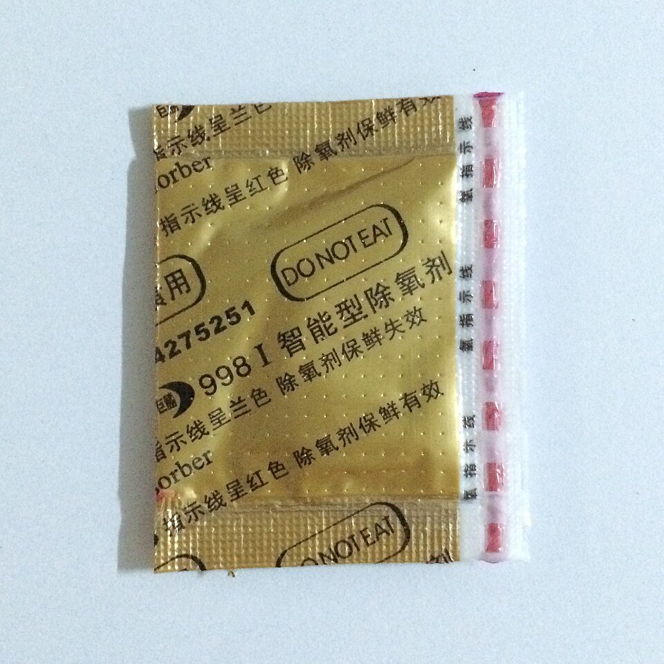 A gold foil oxygen absorber sachet printed with Chinese text and do not eat, with a strip of pink indicator dots down one edge