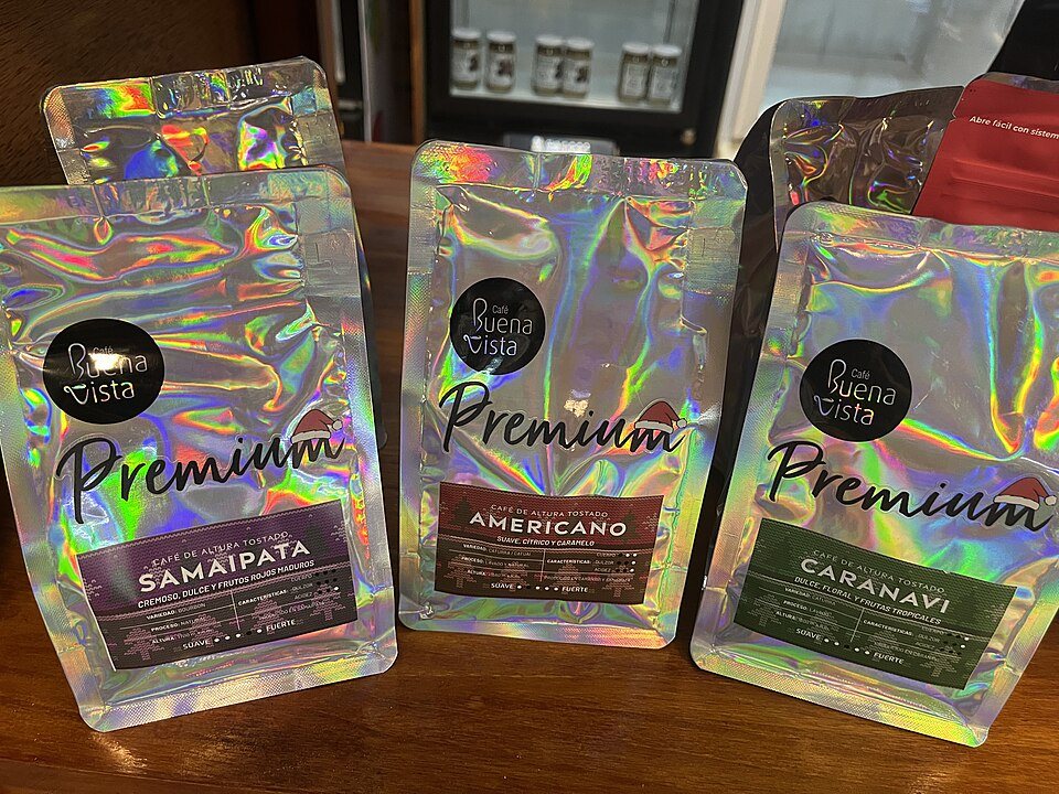 Three stand-up coffee pouches in shiny holographic foil on a table, each with a dark label reading Premium and a different coffee name