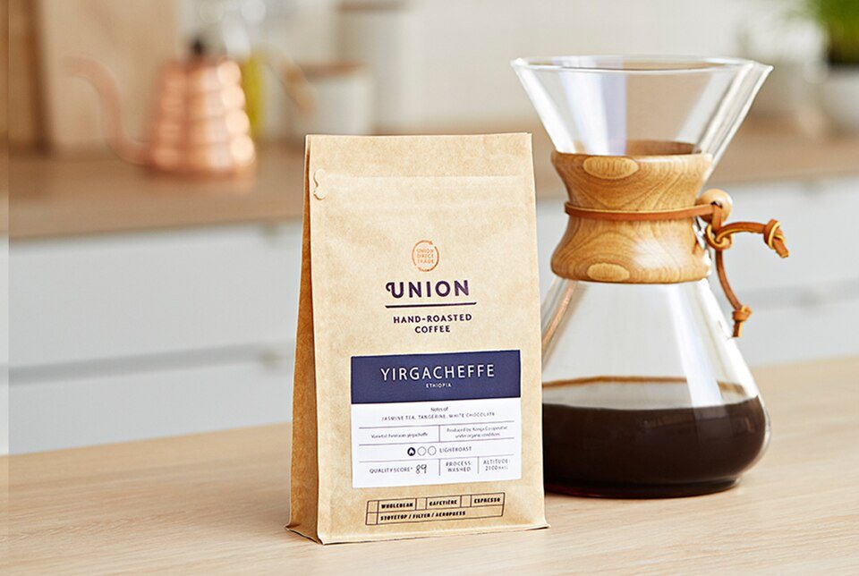 A kraft bag of roasted coffee with a printed label standing beside a Chemex of brewed coffee