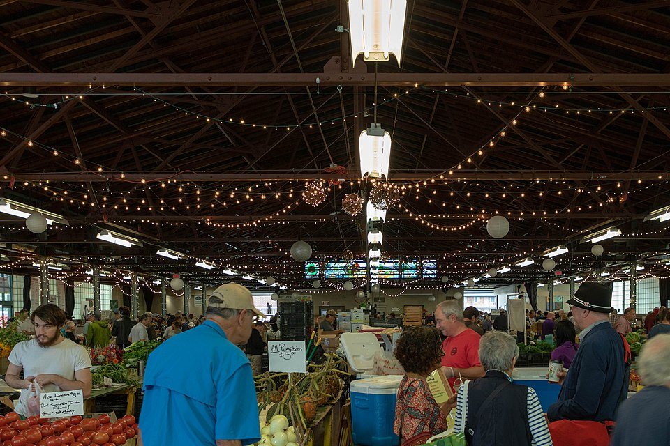 An indoor market hall strung with lights, crowded with shoppers at produce tables