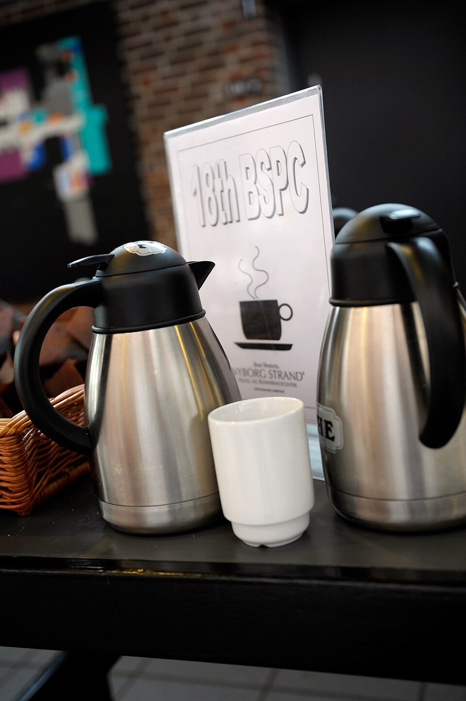 Two stainless thermal carafes and a stack of white cups on a serving table