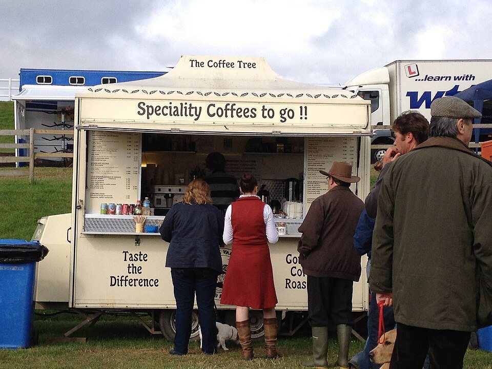 A cream catering trailer signed Speciality Coffees to go, with a queue of people in coats and boots