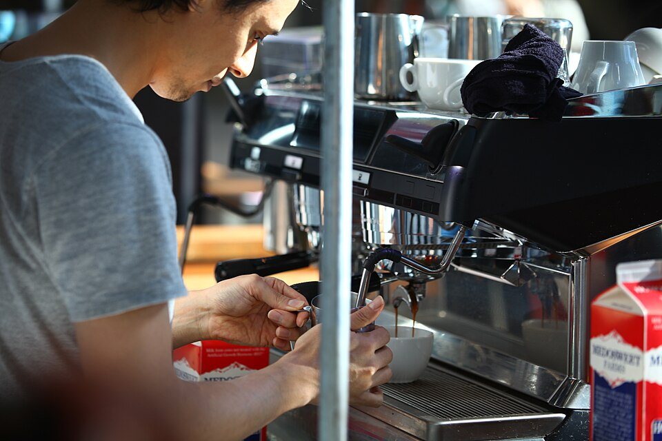 A competitor at an espresso machine working at the group head, a carton of milk beside the machine