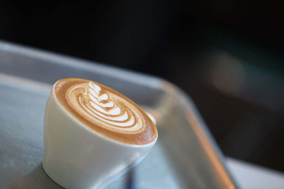 A white cup with a leaf pattern poured in the milk foam, set on a steel tray