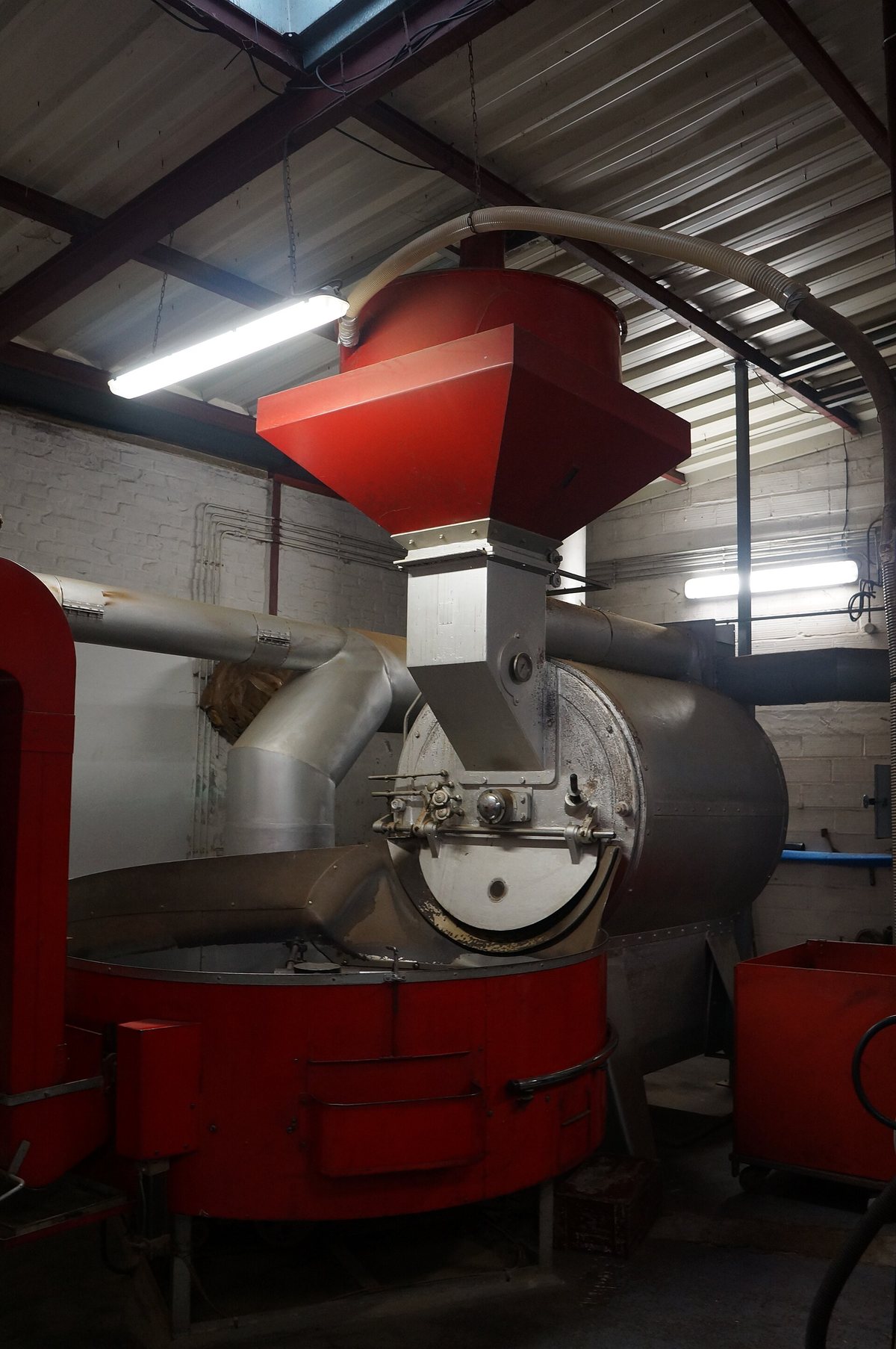 And in a working roastery — the red hopper feeds green in from above, and the ducting takes the smoke away. That ducting is most of the install cost