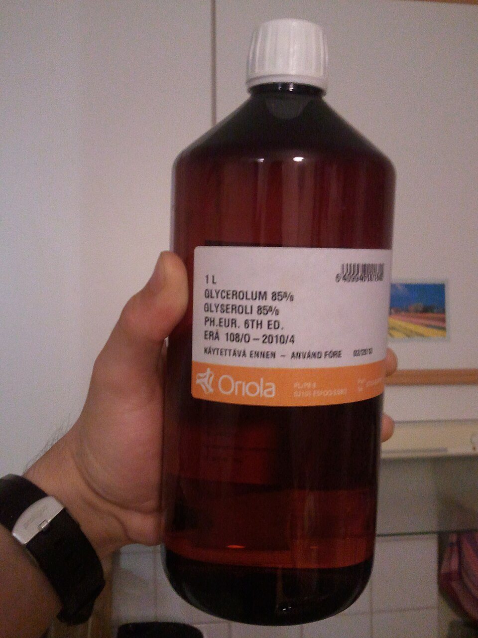 A hand holds a brown plastic litre bottle with a white pharmacy label reading glycerol