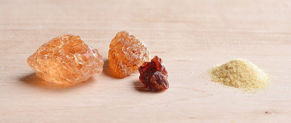Three pale orange translucent lumps of raw gum arabic beside a small heap of cream-colored powder