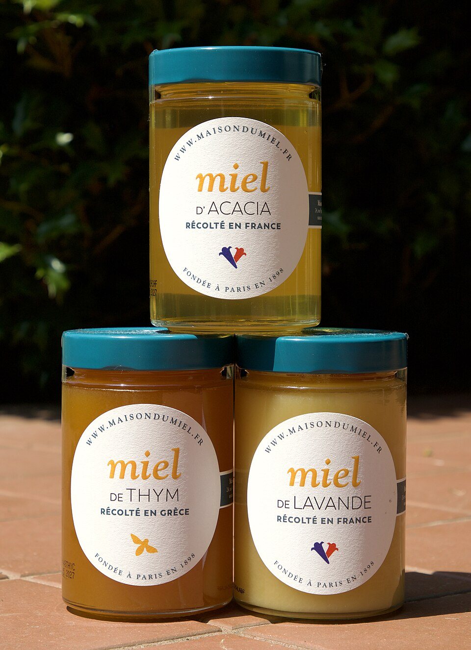 Three jars of honey stacked in a pyramid, labelled acacia, thyme and lavender, each a different shade from pale gold to amber