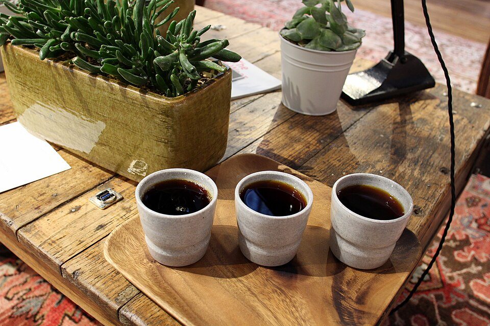 Three handleless ceramic cups of black filter coffee lined up on a wooden board