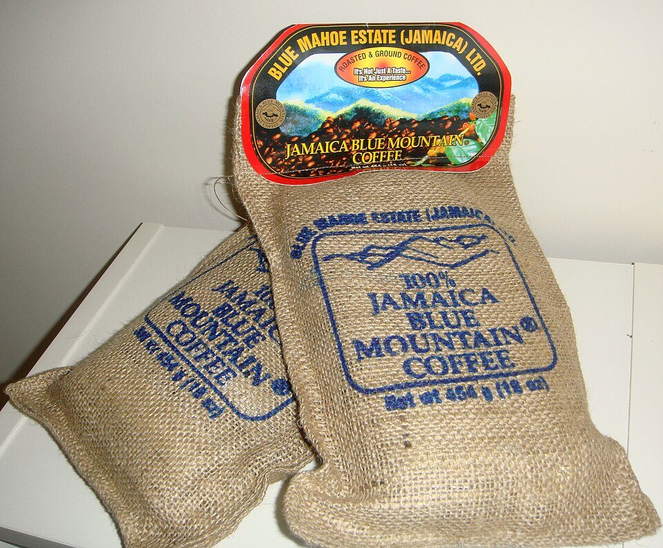 Two small burlap bags printed 100% Jamaica Blue Mountain Coffee, one with a paper estate label