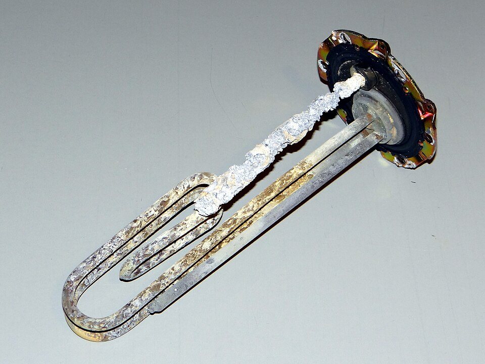 A U-shaped electric heating element removed from a water heater, crusted along its length with pale mineral scale