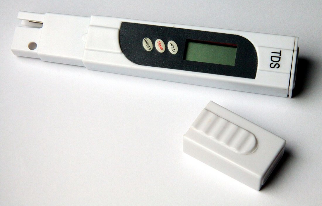 A pen-style TDS meter with its cap off, lying on a white surface
