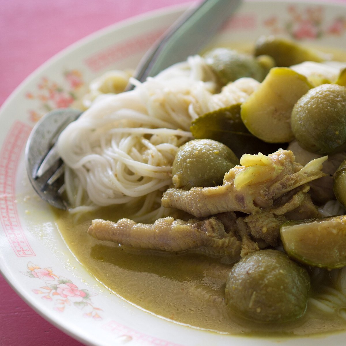 Green curry over khanom chin — fresh rice noodles — with Thai eggplant, makrut lime leaf and chicken feet. Street food, and note how pale the finished curry is