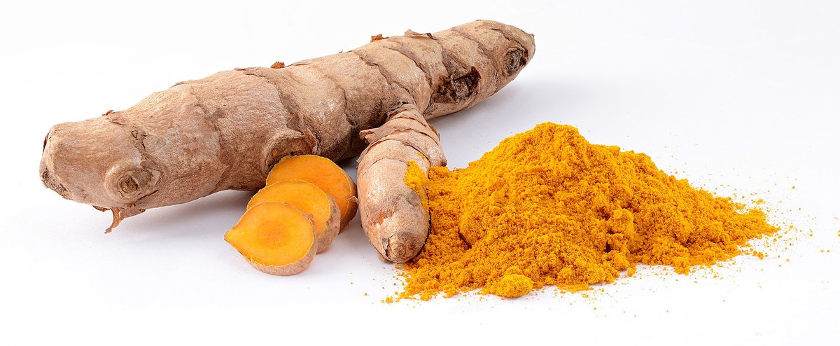 A turmeric rhizome, a cut piece showing the orange interior, and the ground powder beside it