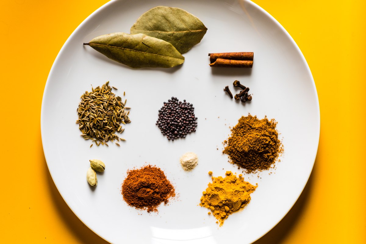 The components laid out separately — bay, cinnamon, clove, cumin, cardamom, mustard, turmeric and chili, before any of them become "curry powder"