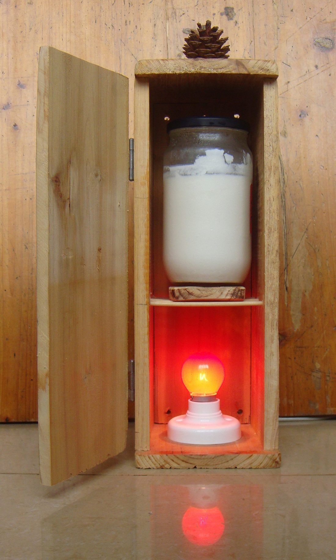 A jar of milk set over a light bulb in a wooden cabinet. This is the whole idea of my first incubator, and it is still a good one