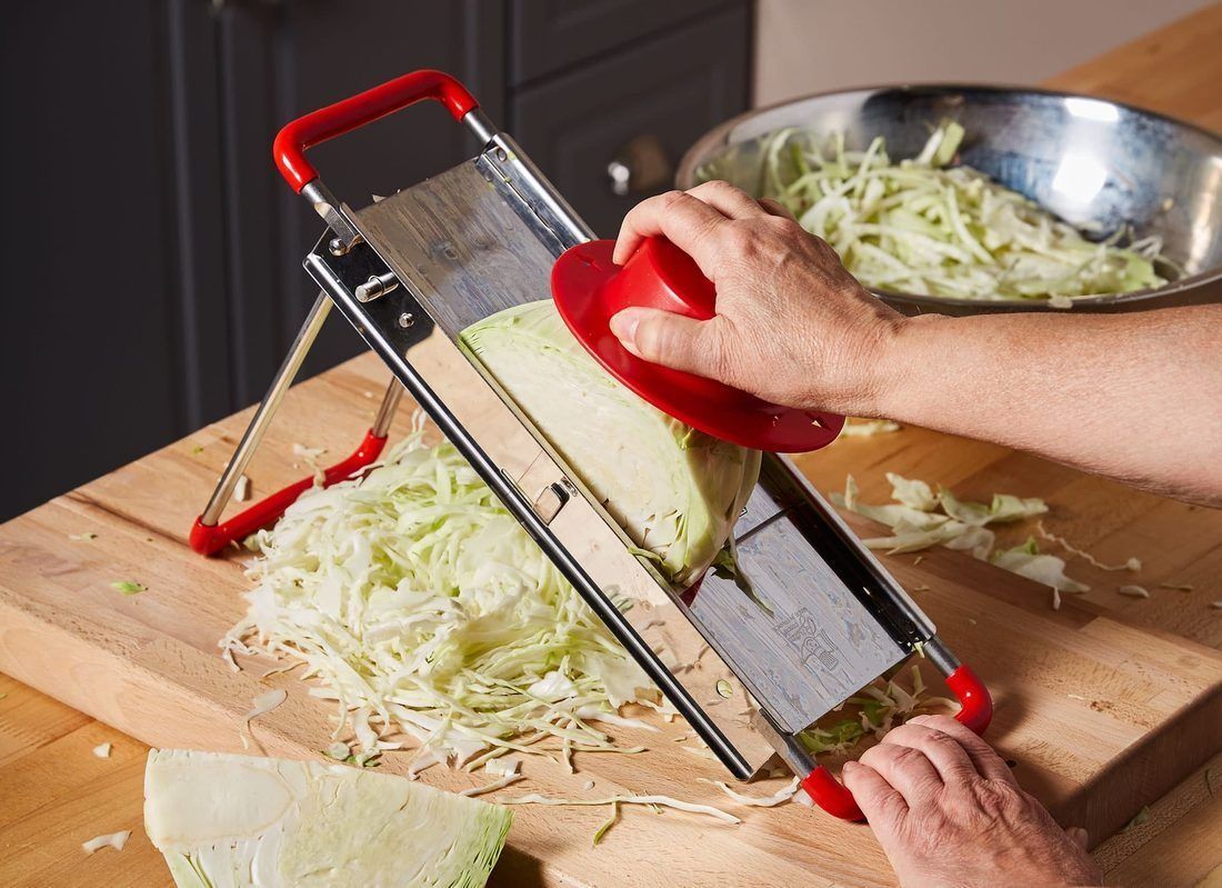 Cabbage going across a mandoline. Consistency matters more than speed — unevenly cut cabbage ferments unevenly