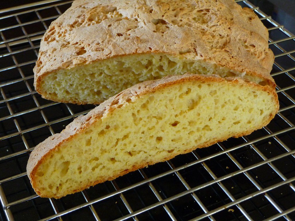 A gluten-free yeast loaf cut in half on a cooling rack, showing a fine yellow crumb