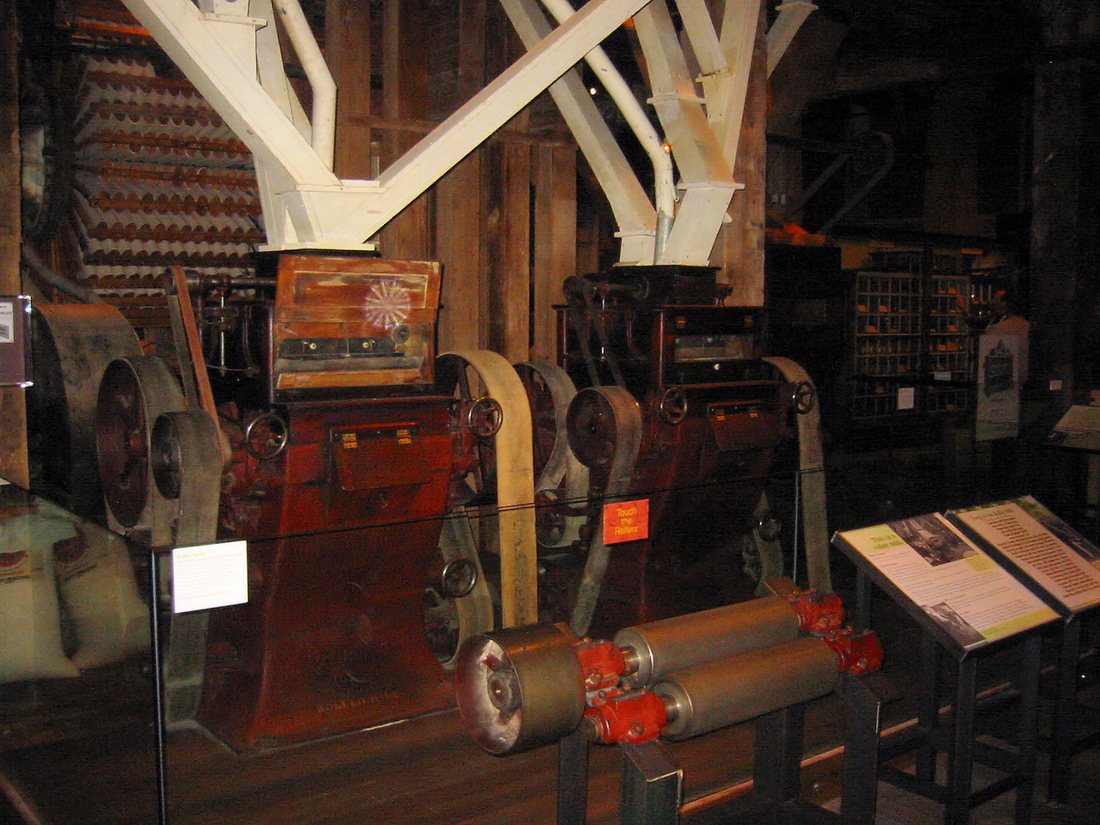 Red cast-iron roller-mill stands under white steel bracing inside the Mill City Museum, with a separated set of rolls displayed in front