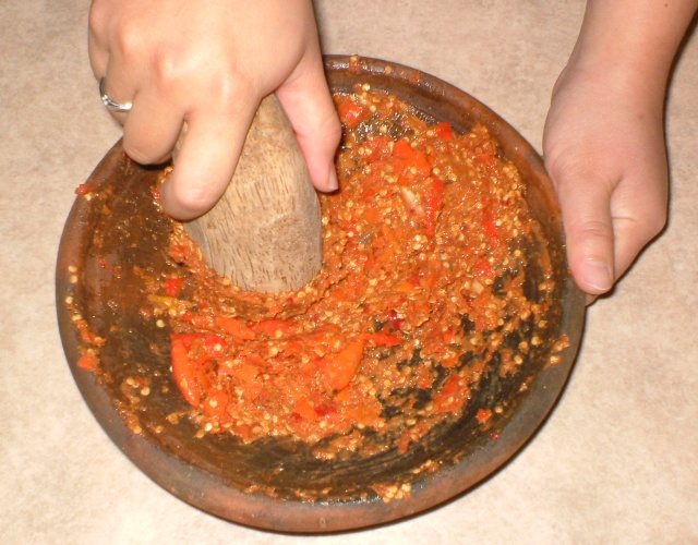 Hands grinding red chiles in a stone mortar with a stone pestle