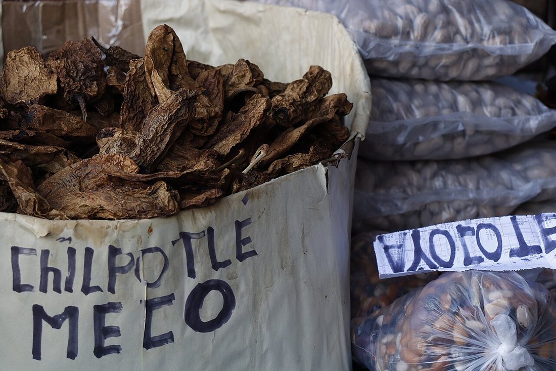 A market sack of dark, leathery dried chiles under a hand-written sign reading Chilpotle Meco