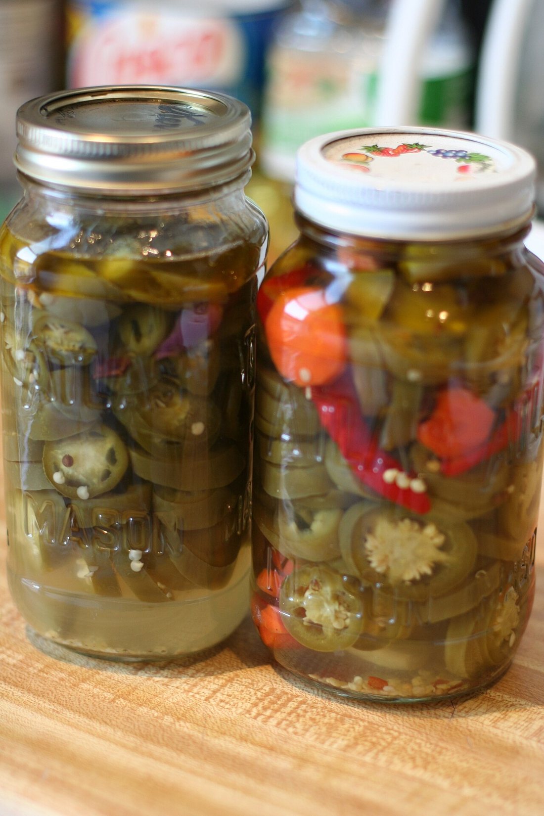 Two jars of pickled sliced jalapeños and red peppers in clear brine