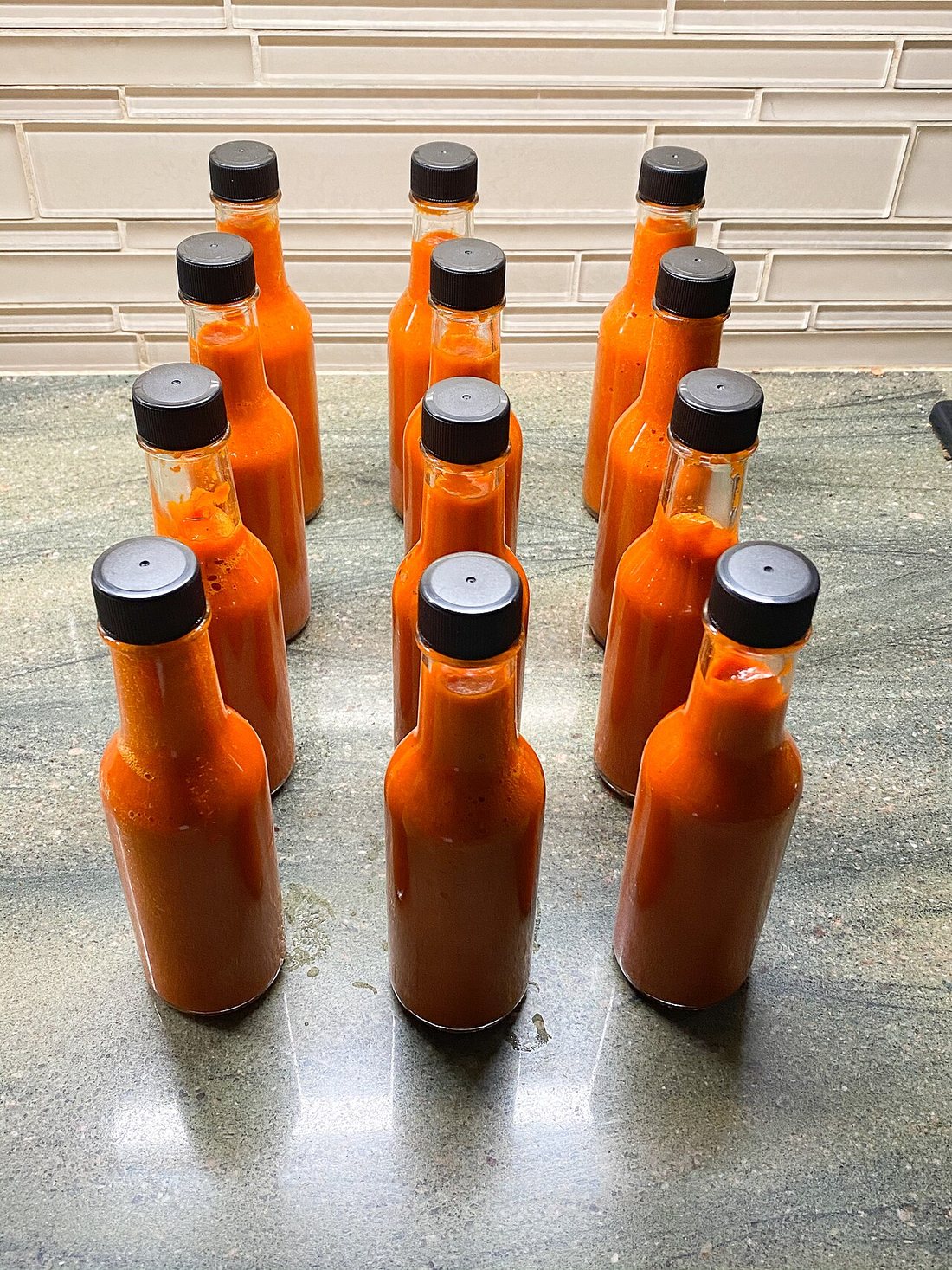 Rows of freshly filled small bottles of orange pepper sauce on a counter