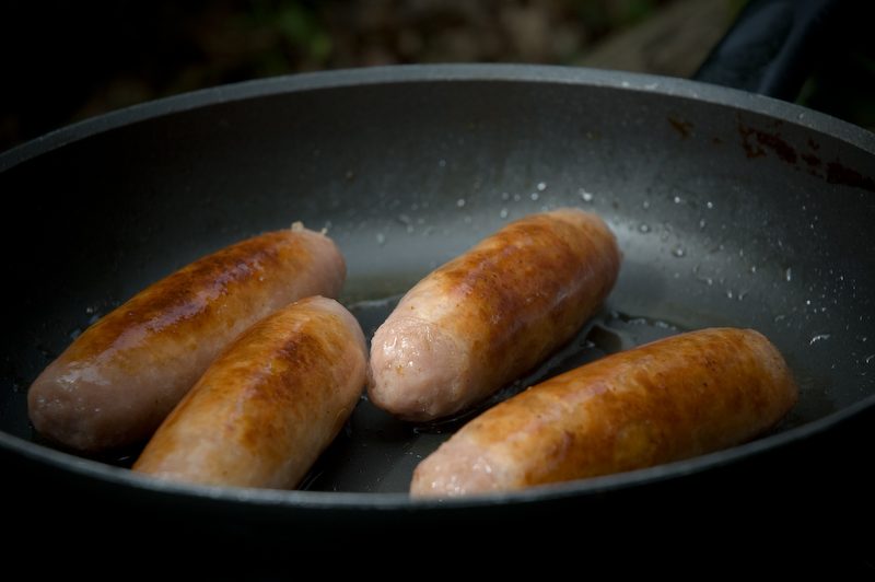 Sausages browning slowly in a frying pan