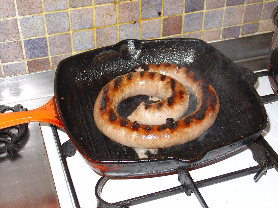 A coil of raw pork sausage in a griddle pan, pale with light browning